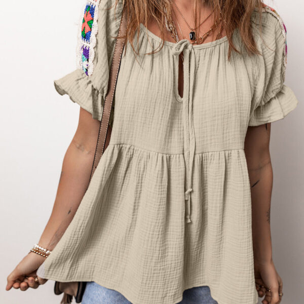 Get ready to be the talk of the town with this one-of-a-kind blouse! Featuring intricate embroidered patches on the sleeves and a chic tied neck detail